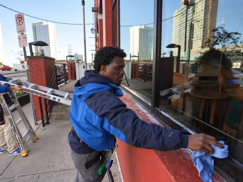 A Camelot window cleaner wiping down a storefront window frame in downtown Nashville