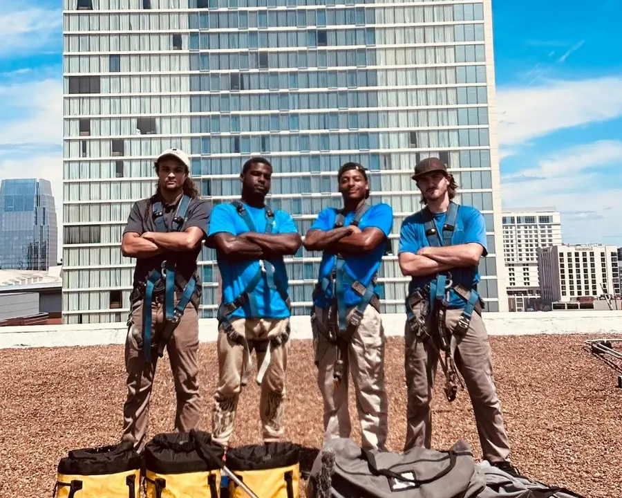 Four Camelot high-rise technicians in rope-access harnesses, arms folded, on a Nashville rooftop with their gear